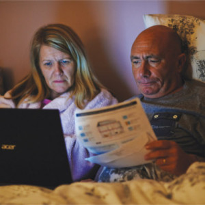 man and wife in bed looking at bills